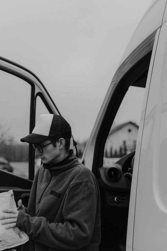 Black and white photo of a courier delivering packages from a van.