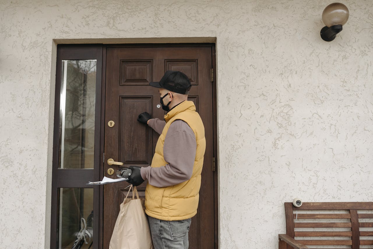 Courier making a contactless delivery at a front door. Wearing mask and gloves.