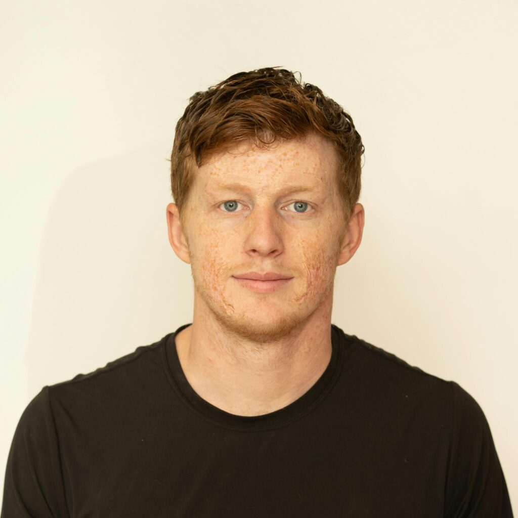 Portrait of a man in a black shirt against a white background, looking directly at the camera.